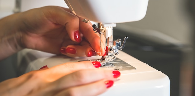 Mulher está colocando linha na máquina de costura. Mãos de meninas em trabalho freelance. Conceito de moda. Criação de novo processo de roupas. Ideias de passatempo.