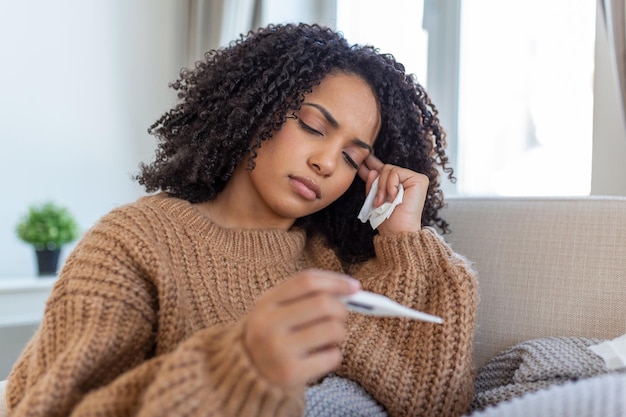 Mulher está com gripe e está usando termômetro doente com rinite mulher pingando nariz Mulher doente com gripe deitada no sofá olhando a temperatura no termômetro