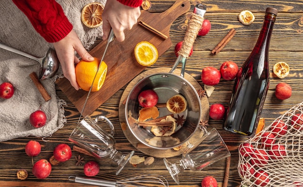 Mulher está cortando laranjas com uma faca para cozinhar vinho quente processo de fazer uma bebida tradicional quente uma atmosfera festiva aconchegante