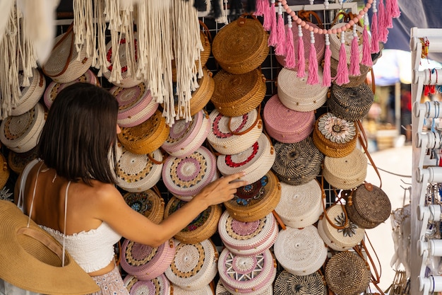 Foto mulher está curtindo sua viagem a um país exótico e entregando um presente entre bolsas de vime em uma pequena loja de rua