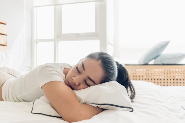 Mulher está dormindo em sua cama branca no apartamento.