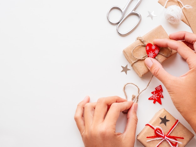 Mulher está embalando presentes de Natal e ano novo DIY em papel ofício. Presentes amarrados com fios brancos e vermelhos.