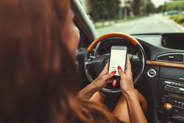 Foto mulher está enviando mensagens de texto no smartphone enquanto dirige um carro e se leva ao perigo.