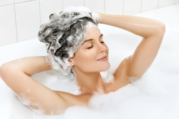 Mulher está lavando o cabelo com shampoo