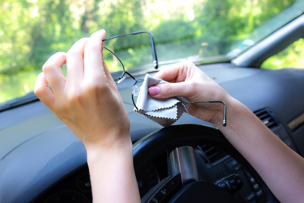 Mulher está limpando os óculos ao volante. Menina dirigindo um carro.