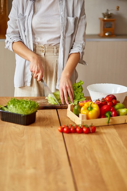 Mulher está preparando salada de legumes na cozinha, cortando folhas de salada