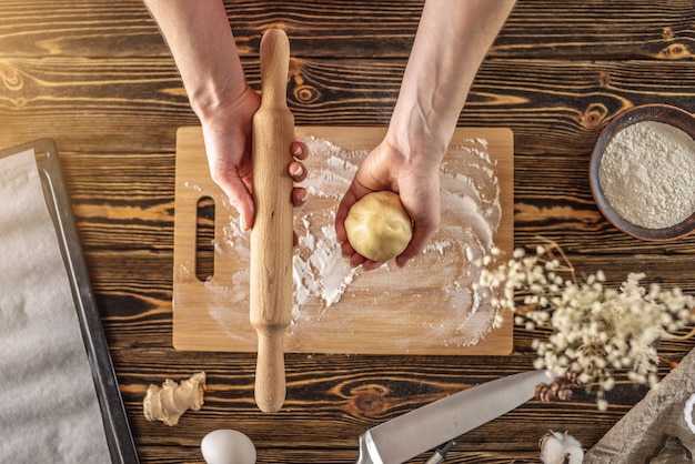 Mulher está segurando massa crua e rolo de massa nas mãos para fazer deliciosos biscoitos de gengibre caseiros em sua cozinha