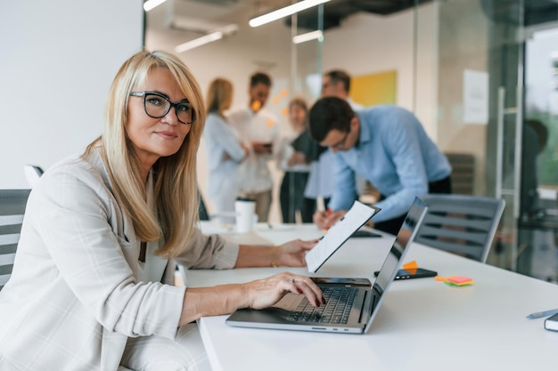 Mulher está sentada à mesa com laptop Grupo de empresários profissionais está no escritório