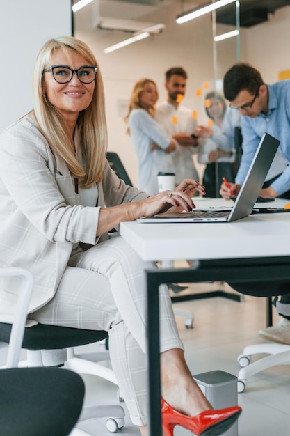 Mulher está sentada à mesa com laptop Grupo de empresários profissionais está no escritório