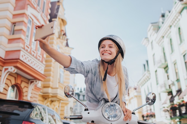 Foto mulher está sentada e inclinando-se para o controle da motocicleta e tomando selfie