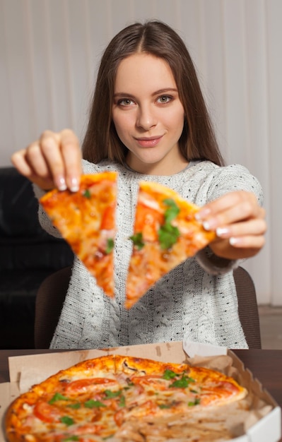 Mulher está sentada e mantendo duas fatias de pizza nas mãos