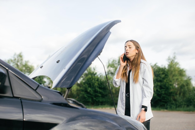 mulher está tendo um problema com um carro que quebrou no caminho e ela abre o capô para verificar