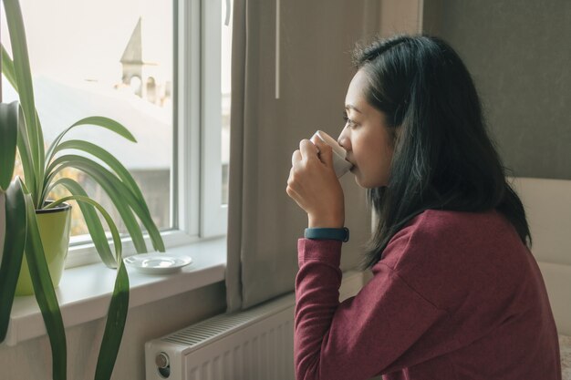 Mulher está tomando café pelas janelas para admirar a vista da cidade.