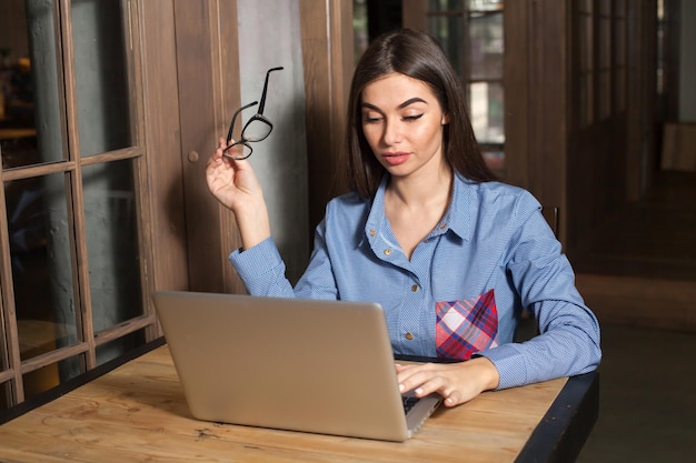 Mulher está trabalhando com laptop e óculos na mão