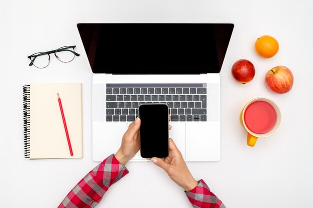 Mulher está usando smartphone com tela em branco sobre a mesa de escritório branco