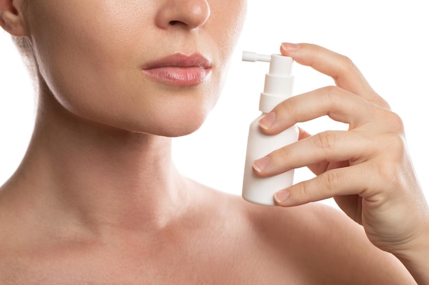 Mulher está usando spray com analgésico para alívio da dor de garganta em fundo branco