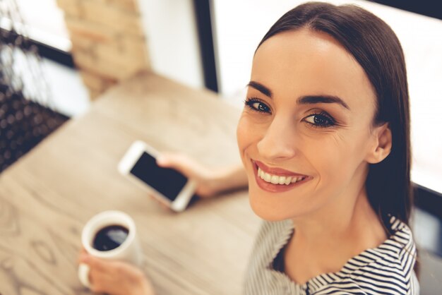 Mulher está usando um smartphone e bebendo café