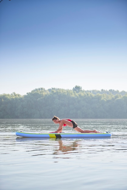 Foto mulher esticando as pernas e as costas em um stand up paddle