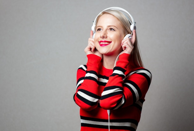 Mulher estilizada com suéter vermelho e fones de ouvido na parede cinza