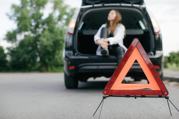 Mulher estressada procurando um carro quebrado e verificando o motor na estrada rural em vista lateral