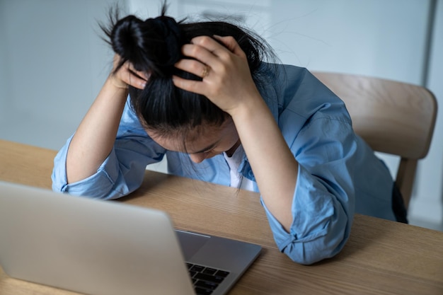 Mulher estressada sentada na mesa com laptop segurando a cabeça nas mãos com problemas de negócios online