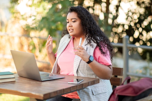 Mulher estudante estudando on-line por meio de videochamada no laptop do lado de fora