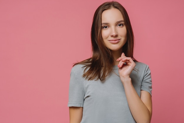 Mulher européia adorável confiante tem pele pura saudável, manicure, vestido com camiseta, goza de sessão de fotos, modelos em rosa