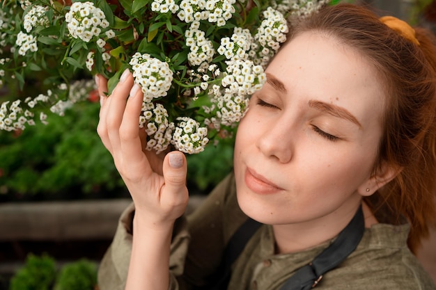 Mulher europeia com cabelo vermelho e olhos fechados, abraçando e cheirando flores brancas no jardim no verão