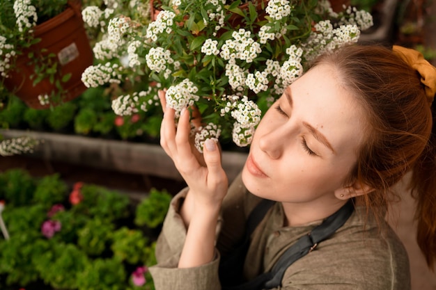 Mulher europeia com cabelo vermelho e olhos fechados, abraçando e cheirando flores brancas no jardim no verão