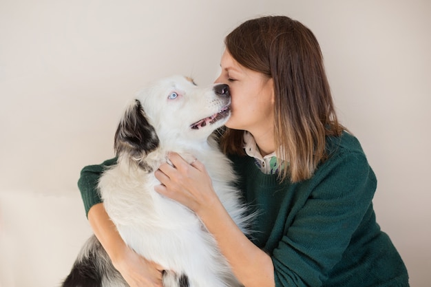 Mulher europeia com jaqueta verde beijando pastor australiano