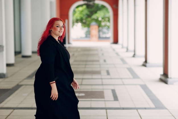 Mulher europeia de tamanho grande andando ao ar livre na cidade de rua Jovem garota positiva de cabelo rosa vermelho