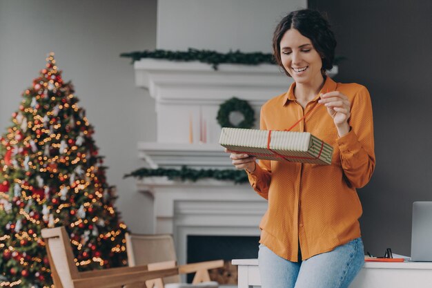 Mulher europeia feliz abrindo presente em uma linda sala de estar decorada de natal