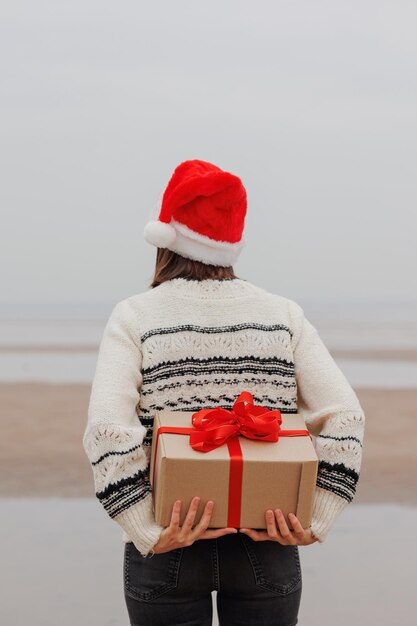 Mulher europeia feliz com chapéu de Papai Noel segurando um presente em uma caixa com uma fita vermelha e seu cachorro labrador