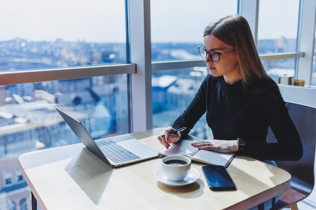 Mulher europeia feliz trabalhando on-line na cafeteria usando laptop e espaço de cópia de café freelancer feminina bem-sucedida digitando no trabalho remoto do laptop