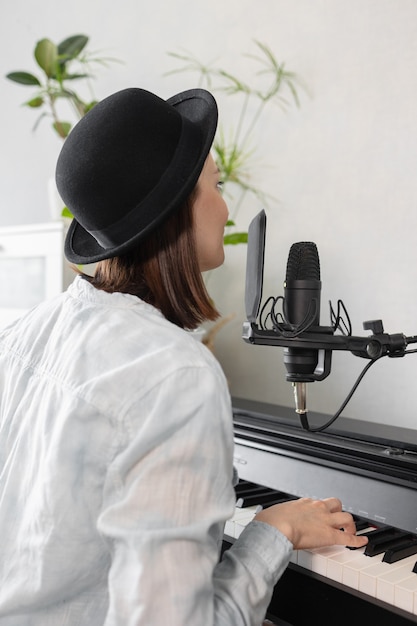 Mulher europeia hipster de chapéu toca piano e canta gravando música e música ou mulher de podcast