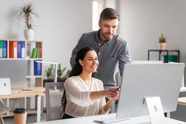 Mulher européia milenar sorridente mostrando ao gerente do homem com a mão na tela do computador