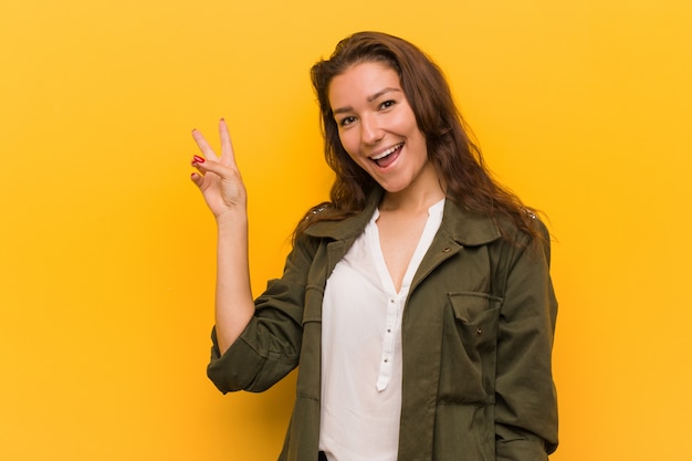 Mulher européia nova isolada sobre o amarelo alegre e despreocupado mostrando um símbolo de paz com os dedos.