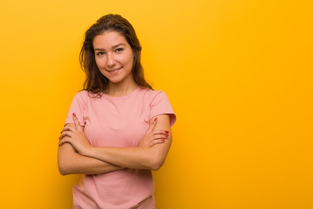 Mulher européia nova isolada sobre o fundo amarelo que sente confiável, cruzando os braços com determinação.