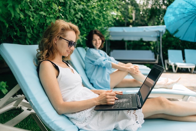 Mulher europeia trabalhando com laptop em férias online Descanso e trabalho no território do hotel com uma namorada turista e freelance de viagens com pc