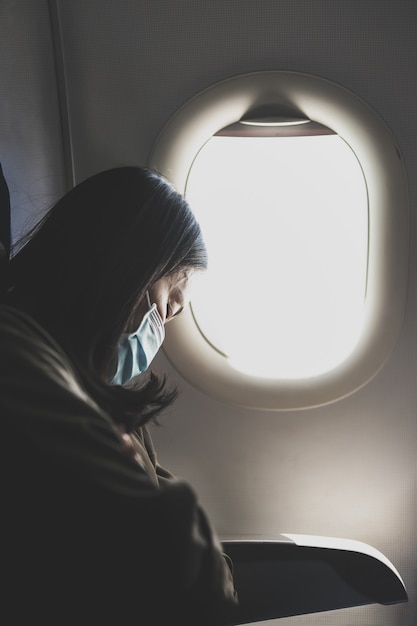 Mulher exausta com máscara protetora dormindo no avião durante a pandemia de coronavírus.