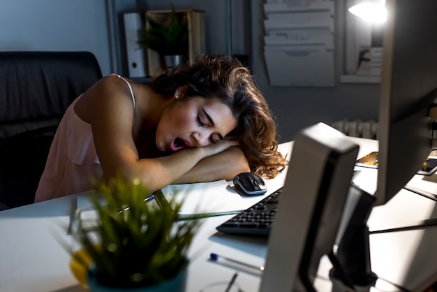 Foto mulher exausta sonolenta que trabalha na mesa de escritório com seu computador, seus olhos estão fechando e