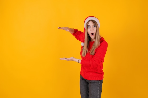 Mulher excitada apontando para o espaço da cópia na mão usando chapéu de Papai Noel e camisola vermelha