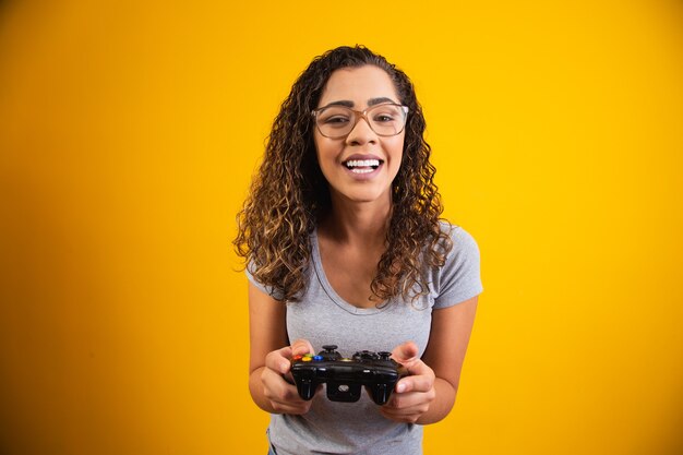 Mulher excitada jogando videogame em fundo amarelo.