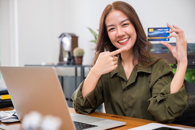 Mulher excitada segurando o cartão de crédito e apontando o cartão preto com computador portátil