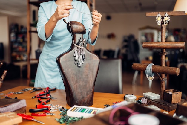 Mulher experimentando colar feito à mão em um manequim de madeira, bordado. artesão feminino no local de trabalho em estúdio de arte