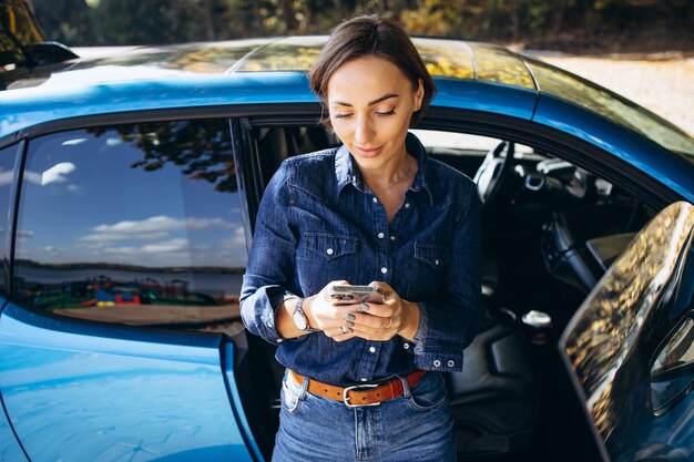 Foto mulher falando ao telefone e de pé perto de seu carro