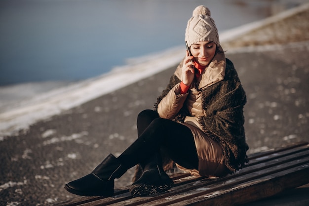 Mulher falando ao telefone e sentada em um banco junto ao lago