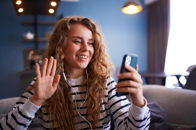 Foto mulher falando em videoconferência com amigos na câmera selfie do smartphone sentada no sofá na sala fofoca de garota em videochamada de casa influenciador cumprimentando seus seguidores