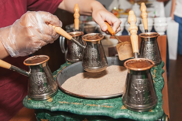 Mulher faz café turco em uma máquina de café com areia em cezve. Café oriental, oriental.