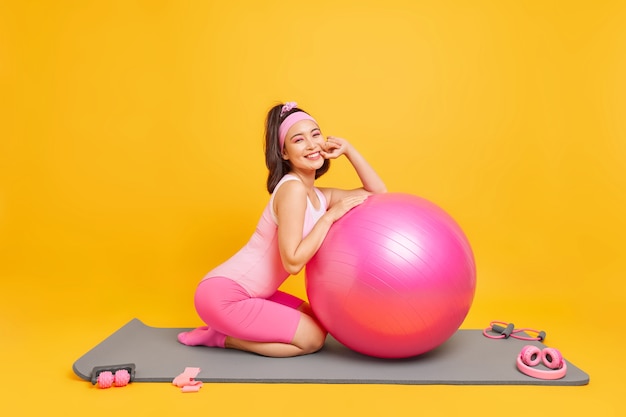 mulher faz exercícios com bola de fitness vestida com roupas esportivas leva estilo de vida ativo saudável usa equipamentos esportivos isolados em amarelo